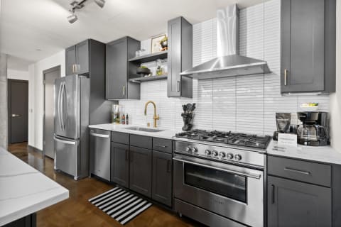 A contemporary kitchen with dark grey cabinets and stainless steel appliances, featuring a brass faucet and white countertops.
