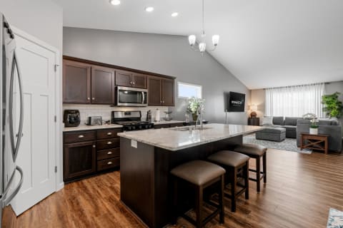A stylish kitchen with dark cabinets and granite countertop connected to a cozy living area with a sectional sofa.