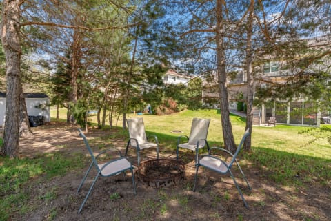 Fire pit with chairs nestled among trees in a backyard.