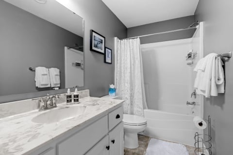 A contemporary bathroom featuring a marble countertop, gray walls, and a white bathtub.