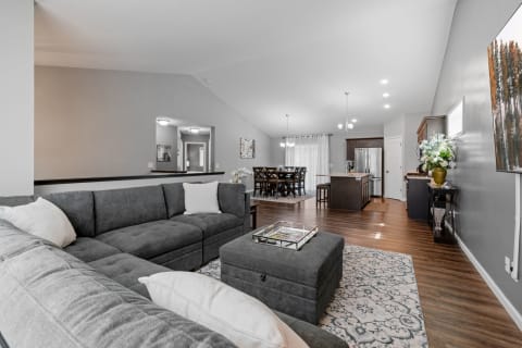 Modern living room featuring a gray sectional sofa, an ottoman, and an open kitchen area.