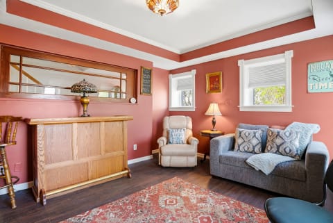 Settle into this cozy living room with warm coral walls, plush seating, and charming vintage touches that invite you to unwind after exploring the area.