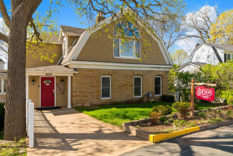 The St. Croix Inn sits in a charming residential neighborhood, featuring distinctive gambrel architecture framed by mature trees and spring greenery.