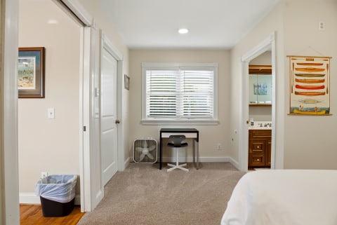 Your bright bedroom features a private workspace and peek into your ensuite, with charming nautical artwork adding coastal character to your serene retreat.