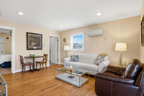 A bright living room featuring a gray sofa, brown leather chair, and a glass coffee table on wood flooring.