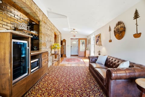 Settle into your cozy living room featuring a plush leather sofa, rustic wood details, and charming nature-inspired artwork. The warm stone accent wall and inviting minibar create the perfect retreat after a day of exploring.