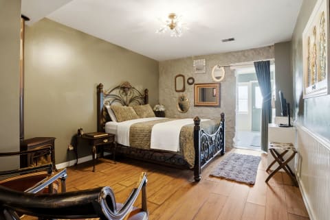 A cozy bedroom featuring a decorative metal bed, vintage furnishings, and a rustic stone wall.