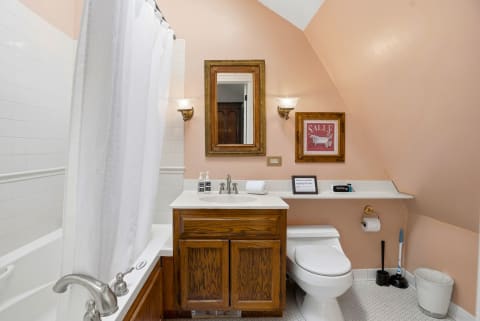 A bathroom with peach walls, white tiles, and a wooden vanity with toiletries.