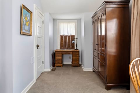 Interior view of a serene bedroom corner with a writing desk, wardrobe, and floral artwork.