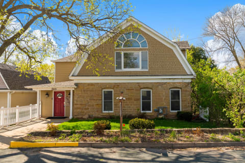 A charming brick property with distinctive arched window details, nestled in a peaceful neighborhood with mature trees and landscaped gardens framing the entrance.