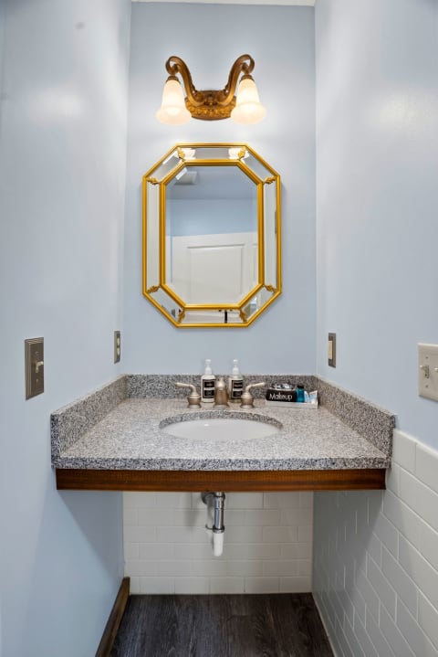 Freshen up at your private vanity, elegantly framed by a golden octagonal mirror and warm vintage lighting, offering a charming touch of style for your daily routine.