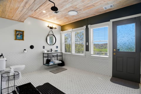 Modern bathroom with rustic wood ceiling, large windows, and sleek fixtures.