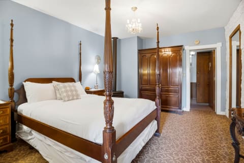 A cozy bedroom with a four-poster bed, wooden wardrobe, and sparkling chandelier under soft blue walls.