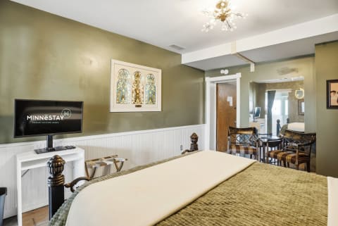 An elegantly decorated bedroom with a king bed, TV, and stained glass window.