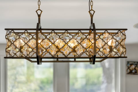 A rectangular bronze chandelier with geometric designs and crystal accents illuminating a room.