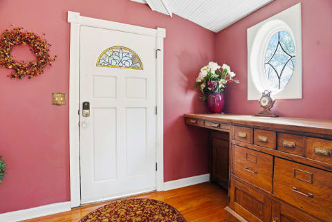 The warm coral walls and decorative wreath welcome you inside, while the vintage dresser and hardwood floors add timeless charm to your entryway.