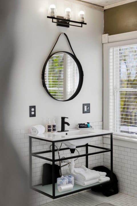Modern bathroom with black metal vanity, subway tiles, and round mirror.