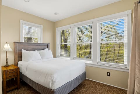 Cozy bedroom with a queen-sized bed, wooden headboard, and large windows overlooking trees.