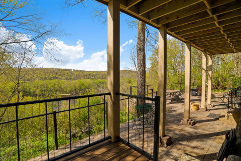 A covered terrace overlooking a green landscape and river, with a clear blue sky above.