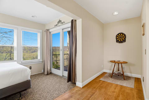 A cozy room featuring a bed, large windows with scenic views, a dartboard on the wall, and a small table.