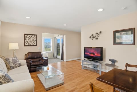 A cozy living room with wood floors, a sofa, a leather chair, and a television.