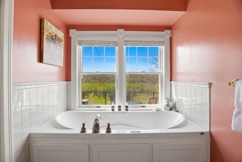 A serene bathroom featuring a white bathtub, coral-painted walls, and large windows showcasing lush green landscapes.