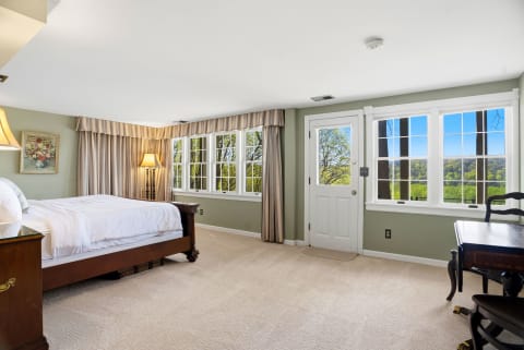 A spacious bedroom with soft linens, elegant furnishings, and large windows overlooking lush scenery.