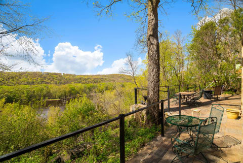 A riverside patio featuring green seating areas and a view of rolling hills and a river.