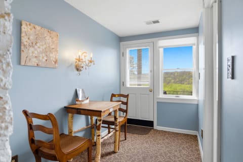 A charming nook with a wooden table and chairs, framed by blue walls and a window showing green hills.