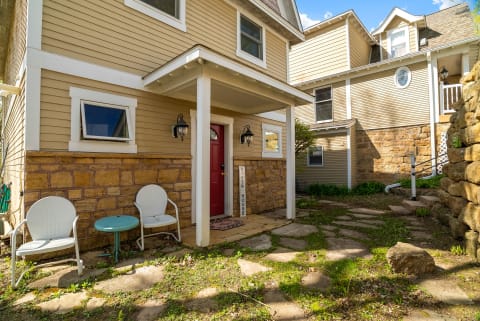Exterior view of a cozy property entrance with stone and siding, featuring a red door and outdoor seating area.