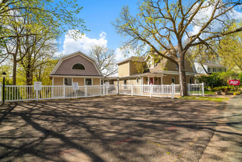 Charming rental property with a picket fence, spacious parking, and lush trees against a blue sky.