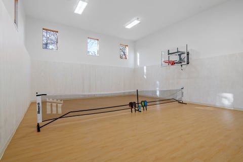 An indoor sports room featuring a basketball hoop and a badminton net with colorful paddles.