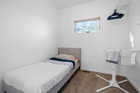 A simple bedroom featuring a bed with colorful bedding and a white bassinet.