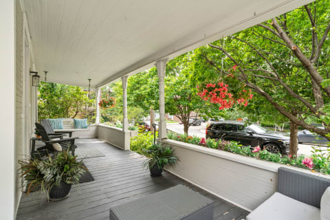 A charming front porch with a rocking chair and swing surrounded by greenery and flowers.