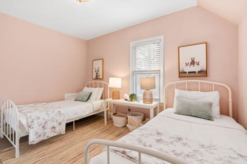 Cozy pink bedroom featuring two beds, soft lighting, and a playful bear artwork.