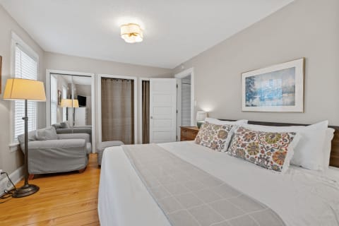 Cozy bedroom with large bed, decorative pillows, and a gray armchair.