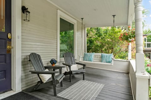 A cozy porch setup featuring two chairs, a swing, and decorative plants.