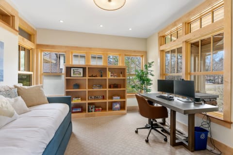 Home office with large windows, a blue daybed, and a modern desk setup with two monitors.