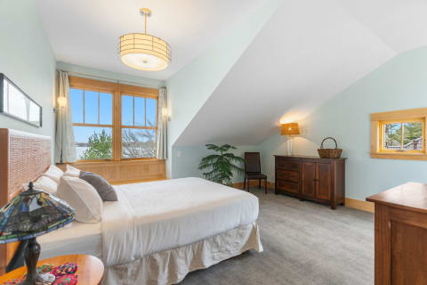 Cozy bedroom with angled ceiling, large windows, and wooden furnishings.