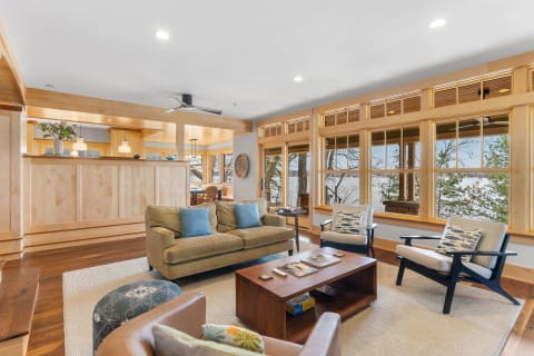 A modern living room with large windows, olive-green couch, and wooden furniture.