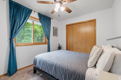 A bright, cozy bedroom with a gray bedspread, teal curtains, and a wooden closet.
