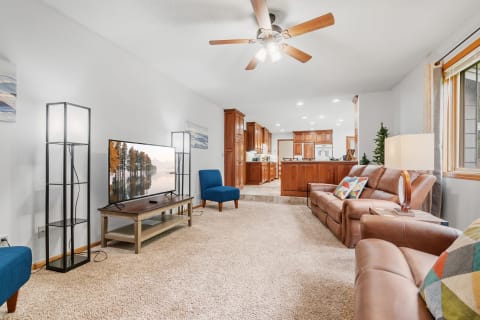 Cozy living room with leather couch, blue chair, and open kitchen area in the background.