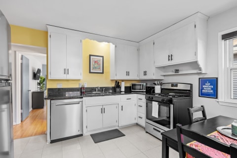 Modern kitchen with white cabinets and black countertops, yellow walls, and a dining table.