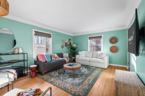 A cozy living room featuring a mint green wall, colorful pillows, and a patterned area rug.