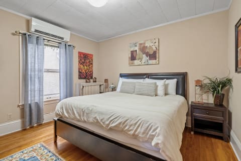 A cozy bedroom featuring a large bed, colorful artwork, and natural light from a window.