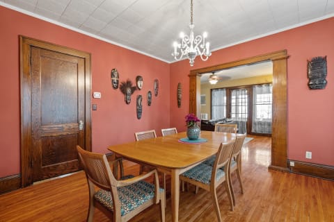 Interior view of a dining room featuring a wooden table, decorative masks on the wall, and a chandelier.