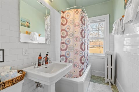 Bright bathroom with white tiles, colorful shower curtain, and a vintage radiator.