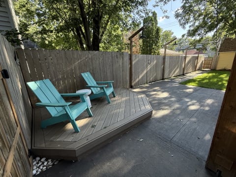 Turquoise adirondack chairs on a wooden deck in a peaceful backyard setting.