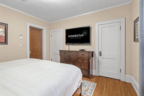 Interior view of a cozy bedroom with a bed, wooden dresser, and a TV on the wall.