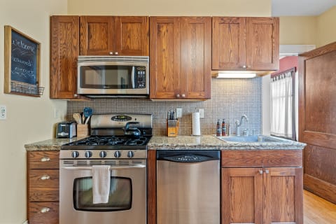 A modern kitchen with oak cabinets, a gas stove, and stainless steel appliances, decorated with a chalkboard message.